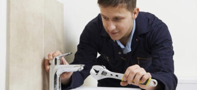 Male Plumber Working On Sink Using Wrench