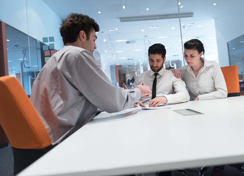signing contract on partners back, young couple on business meeting with life insurance and bank loan agent at modern office interior
