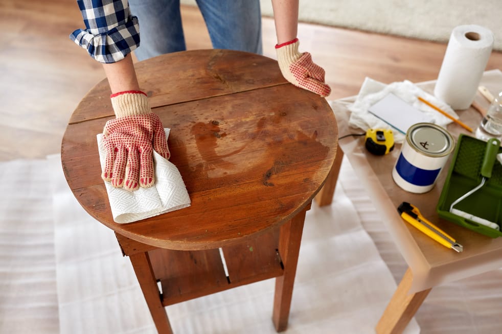 furniture renovation, diy and home improvement concept - close up of woman cleaning or degreasing old round wooden table surface with paper tissue