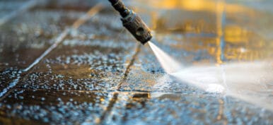 This macro photograph captures the intense cleaning power of a pressure washer as it meticulously cleans a paved yard. The focused stream of water removes dirt and grime, revealing the clean surface beneath.